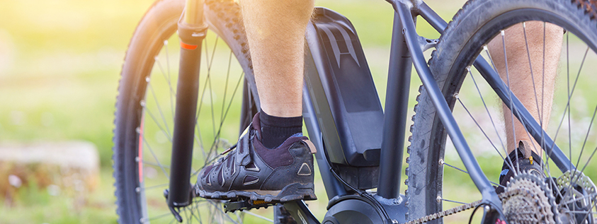 E-Bike-Touren Person, die an einem sonnigen Tag ein schwarzes E-Bike fährt, Nahaufnahme der Pedale und des Hinterrads.