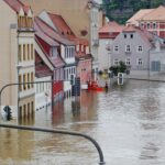 Überflutete Straße mit untergetauchten Gebäuden und einem Rettungsboot, das Menschen hilft.