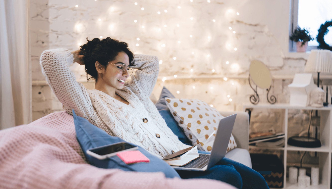 Frau sitzt gemütlich am Bett mit ihrem Laptop am Schoß